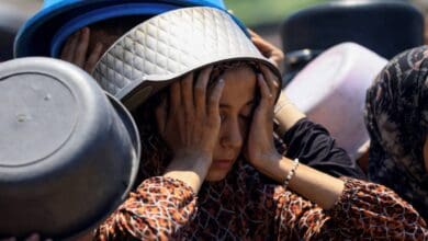 A Palestinian girl, with a cooking pot on her head for shade, rests her face in her hands while waiting in a long queue to receive food in Gaza City.