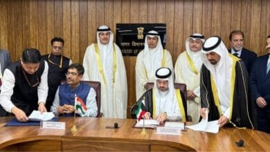 Officials from India and Kuwait sign a bilateral air services agreement in New Delhi, seated at a wooden conference table with national flags and nameplates.