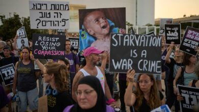 Israeli activists protest in Tel Aviv against the Gaza war, food restrictions, and forced displacement of Palestinians. Demonstrators hold signs reading “Starvation is a war crime” and “Resist losing your compassion,” alongside images of malnourished children.