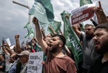 Protesters shout slogans and wave flags during a demonstration against LeMan magazine in Turkey, holding signs with strong messages.
