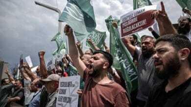 Protesters shout slogans and wave flags during a demonstration against LeMan magazine in Turkey, holding signs with strong messages.
