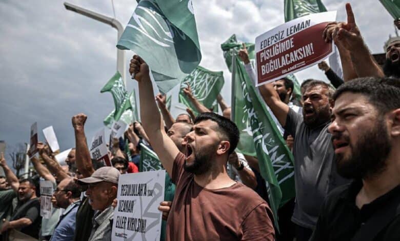 Protesters shout slogans and wave flags during a demonstration against LeMan magazine in Turkey, holding signs with strong messages.