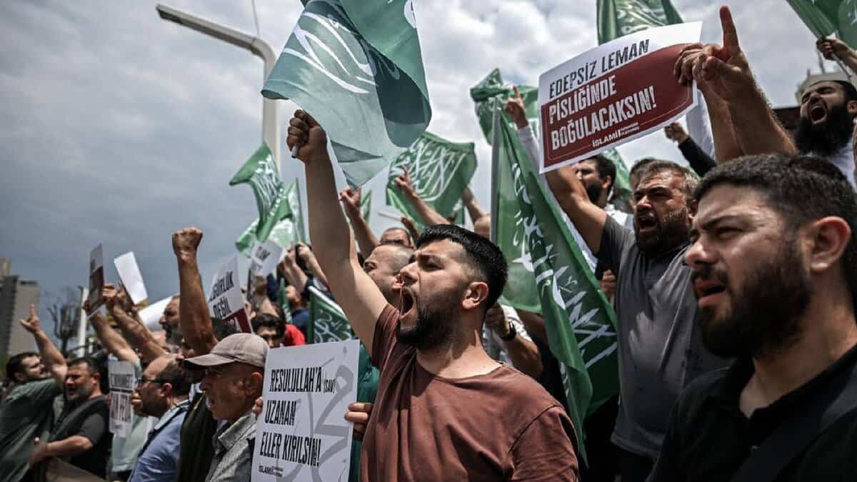 Protesters shout slogans and wave flags during a demonstration against LeMan magazine in Turkey, holding signs with strong messages.