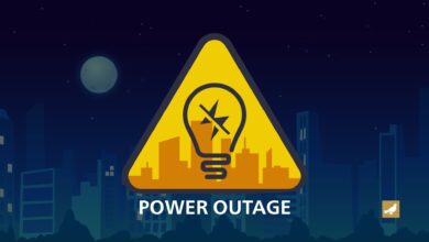 Illustration of a power outage warning, featuring a yellow triangular caution sign with a broken light bulb symbol in front of a city skyline at night.