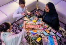 The image of a thrree people, including a child and two women, play the newly launched Riyadh edition of Monopoly at a modern indoor setting.