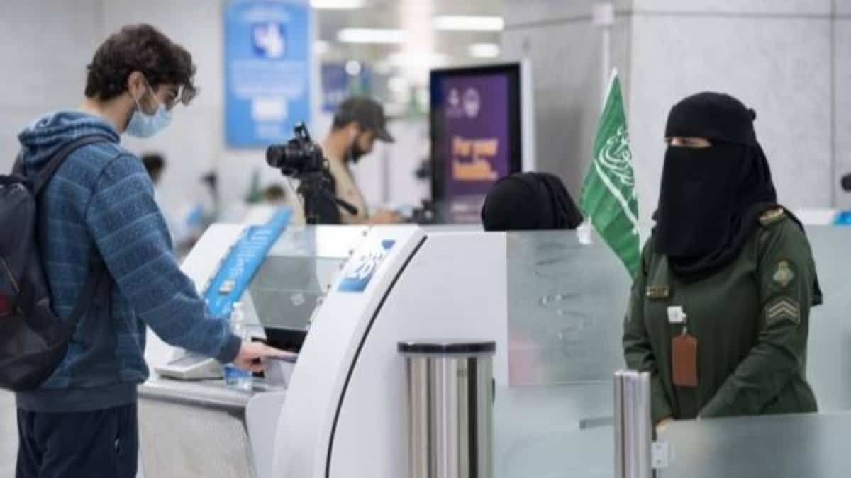 A Saudi female immigration officer in uniform processes a male passenger at an airport immigration counter.