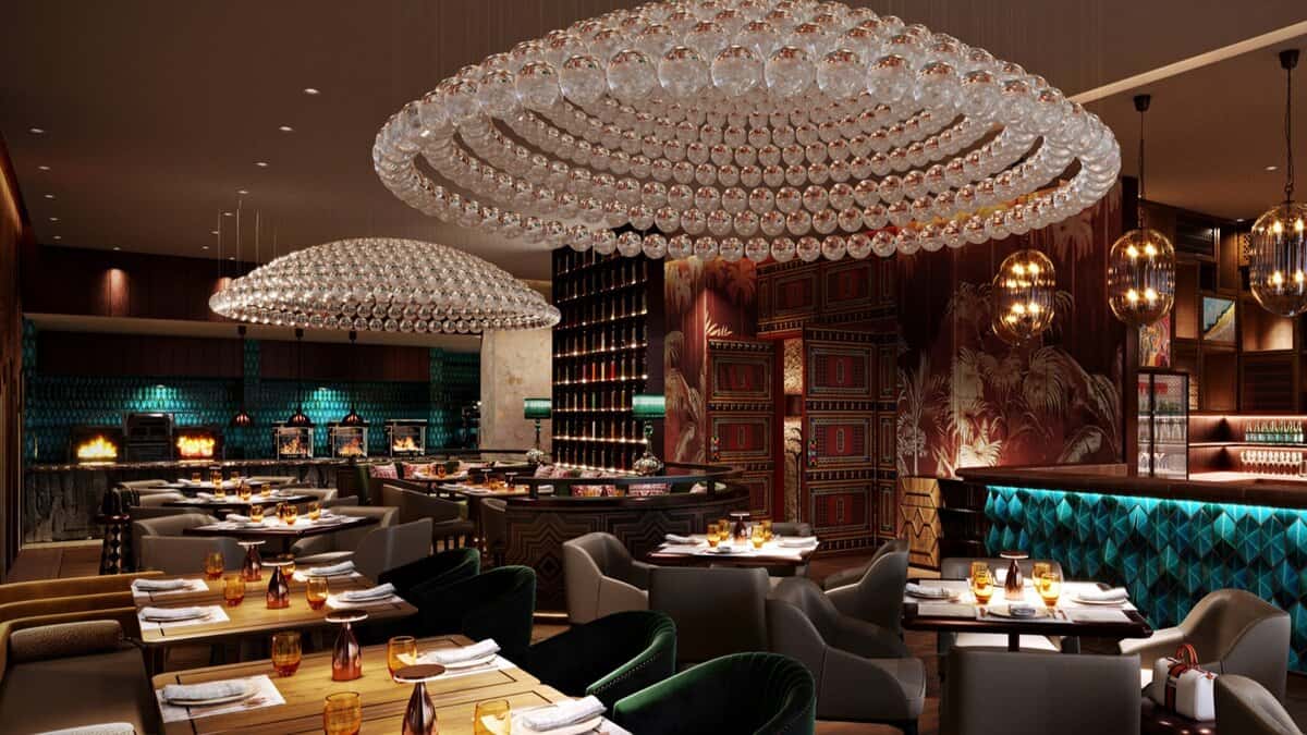 Luxurious interior of a Saudi café featuring elegant crystal chandeliers, plush seating, rich wood and patterned wall decor, with teal and gold accents. Tables are neatly set with amber glassware and napkins, creating a warm and upscale dining ambiance.