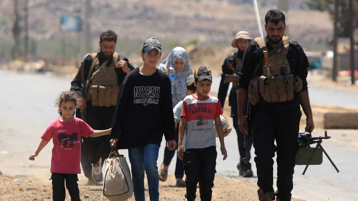 A Syrian family walks with armed escorts during displacement from Sweida.