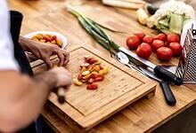 Chef chopping fresh cherry tomatoes on a wooden board with vegetables and kitchen tools around.