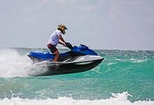 A person rides a jet ski over waves in the sea, wearing a helmet and safety gear.
