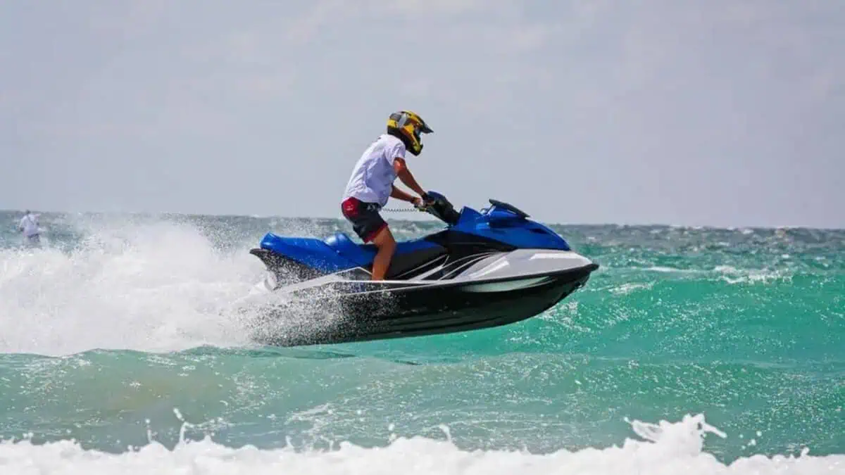 A person rides a jet ski over waves in the sea, wearing a helmet and safety gear.