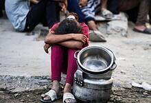 Child sits beside empty cooking pots while waiting for food in Gaza City.