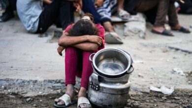 Child sits beside empty cooking pots while waiting for food in Gaza City.