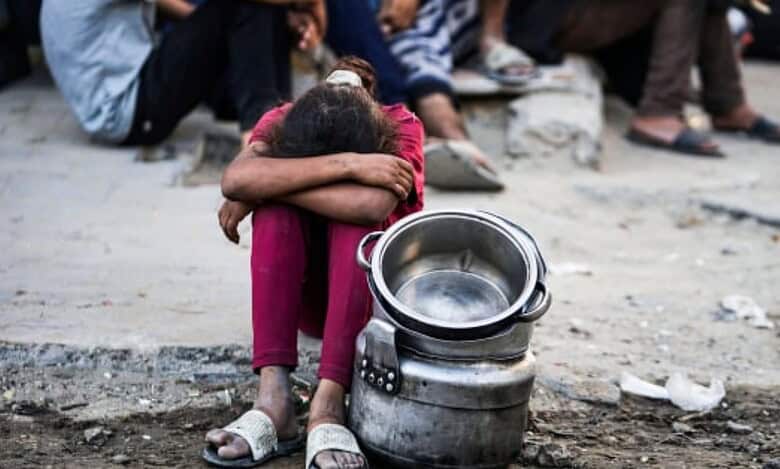 Child sits beside empty cooking pots while waiting for food in Gaza City.