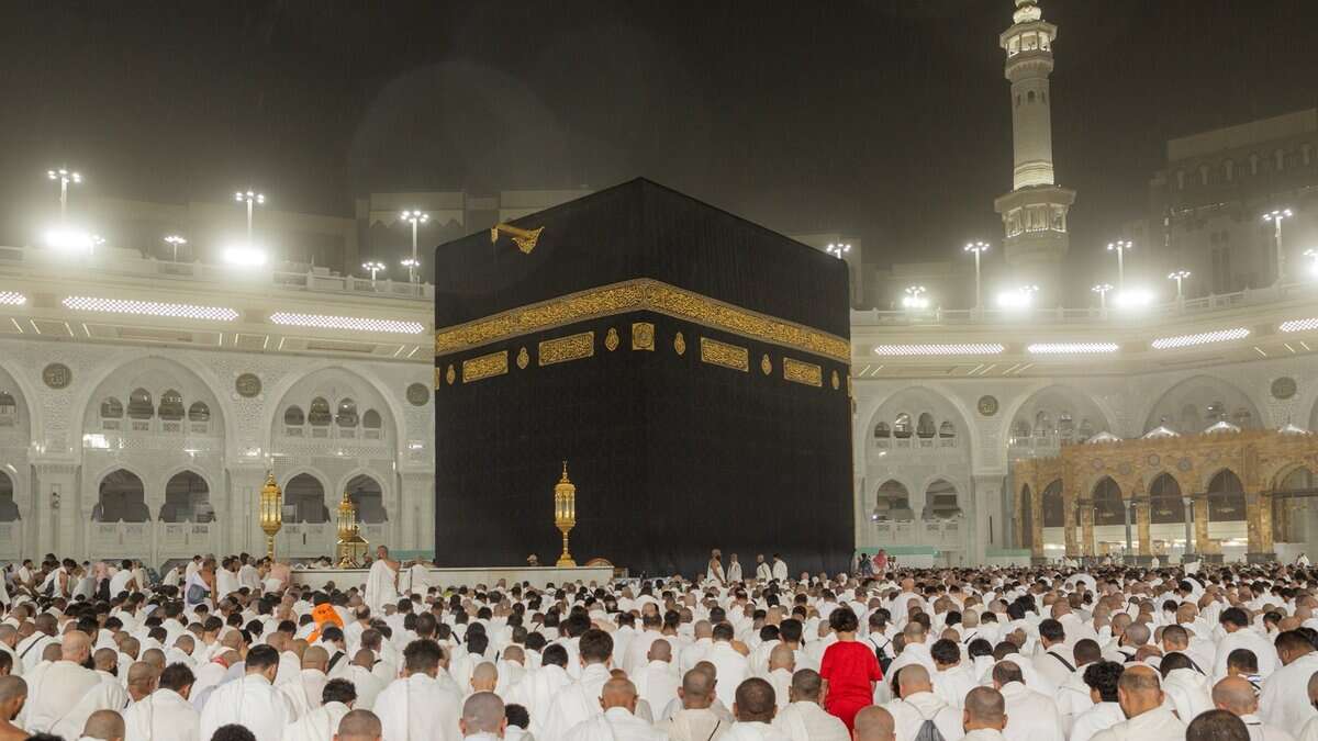 Pilgrims in white Ihram gather at the Grand Mosque in Makkah, surrounding the Kaaba in prayer under bright lights during a sacred moment of worship.