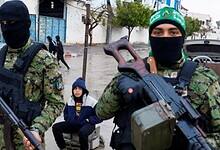 Armed Hamas militants in camouflage and masks stand guard on a street in Gaza.