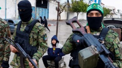 Armed Hamas militants in camouflage and masks stand guard on a street in Gaza.