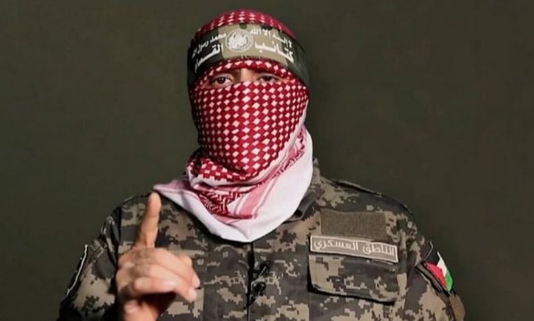 Abu Obeida, Hamas military spokesman, appears in military uniform with a red keffiyeh covering his face during a televised statement.