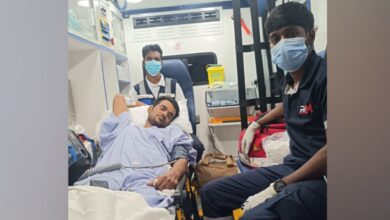 Anilkumar V is seen on a stretcher inside an ambulance, receiving medical assistance during his repatriation to India, accompanied by two paramedics.