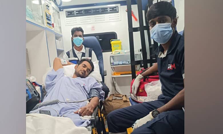 Anilkumar V is seen on a stretcher inside an ambulance, receiving medical assistance during his repatriation to India, accompanied by two paramedics.