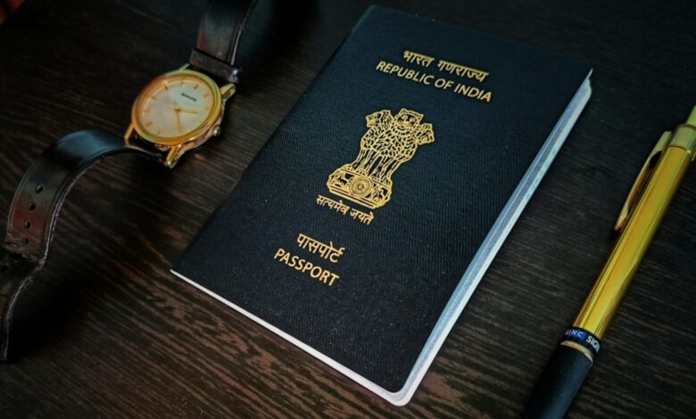 Indian passport placed on a dark wooden table with a wristwatch and a golden pen.