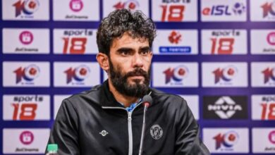 The image shows Khalid Jamil, a man with a beard and curly hair, wearing a black jacket with a logo, sitting at a press conference with microphones, surrounded by ISL and sponsor banners.