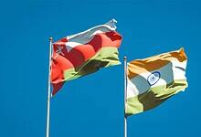 National flags of Oman and India waving against a clear blue sky, symbolising diplomatic and trade relations between the two nations.