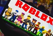 A group of Roblox characters standing on grass, displayed on a phone screen with the "ROBLOX" logo prominently shown.