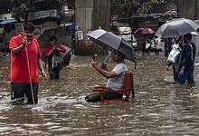 A man sits on a chair as people wade through a waterlogged road amid rainfall in Mumbai on Tuesday. (PTI Photo)