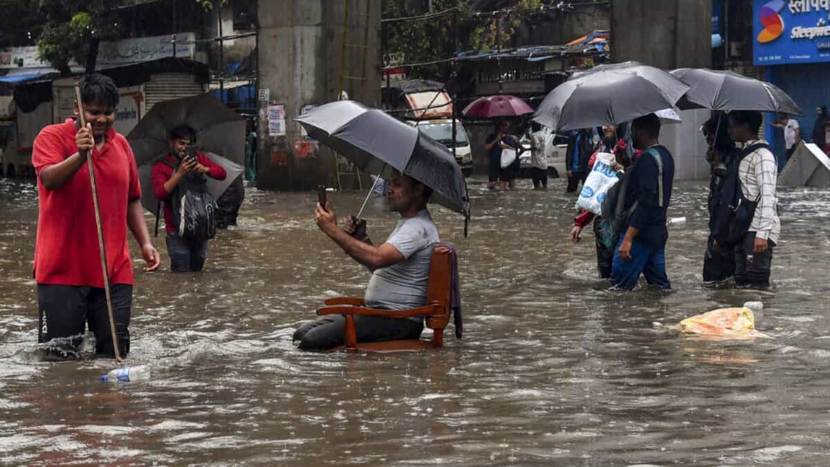 A man sits on a chair as people wade through a waterlogged road amid rainfall in Mumbai on Tuesday. (PTI Photo)