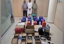 Boxes and containers of oil with seized narcotics displayed by Abu Dhabi Police alongside three arrested suspects.