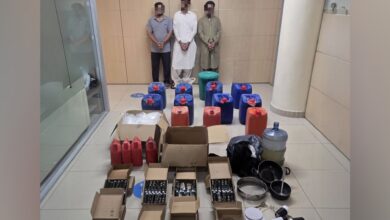 Boxes and containers of oil with seized narcotics displayed by Abu Dhabi Police alongside three arrested suspects.