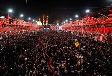Crowds of Shiite worshippers gather in Karbala, Iraq, during the Arbaeen pilgrimage at night, with illuminated shrines in the background.