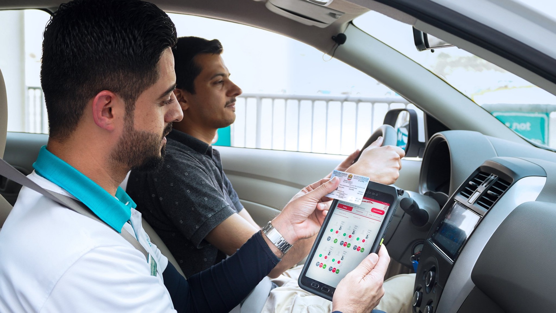 Driving instructor using tablet to assess trainee driver in Dubai.