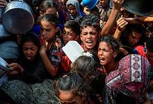 A crowded scene of people, mostly children, holding pots and containers, reaching out in a desperate manner.