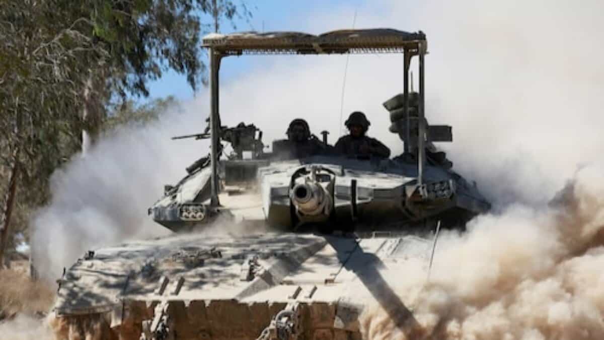 A military tank moving through a dusty environment with two soldiers visible in the turret.