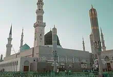 A view of the Prophet’s Mosque in Madinah, Saudi Arabia, with its iconic green dome and minarets under a clear sky.