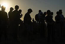 Silhouettes of Orthodox Jewish men standing together at sunset near the Gaza border.