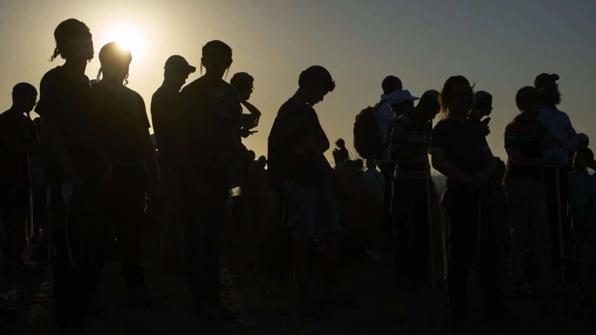 Silhouettes of Orthodox Jewish men standing together at sunset near the Gaza border.