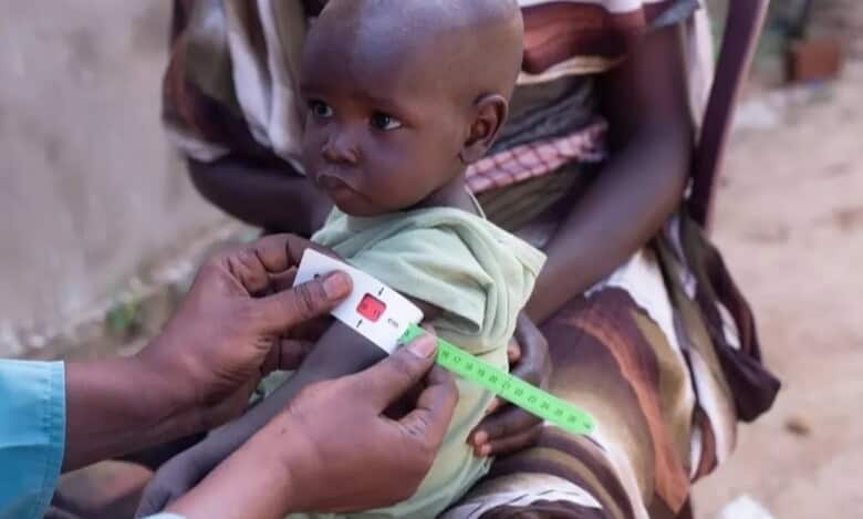 A young child receiving a health check-up, being measured for vaccination or nutritional assessment in a rural setting.