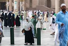 Bustling courtyard of Prophet's Mosque in Madinah with Umrah pilgrims and a cleaner amid iconic architecture.