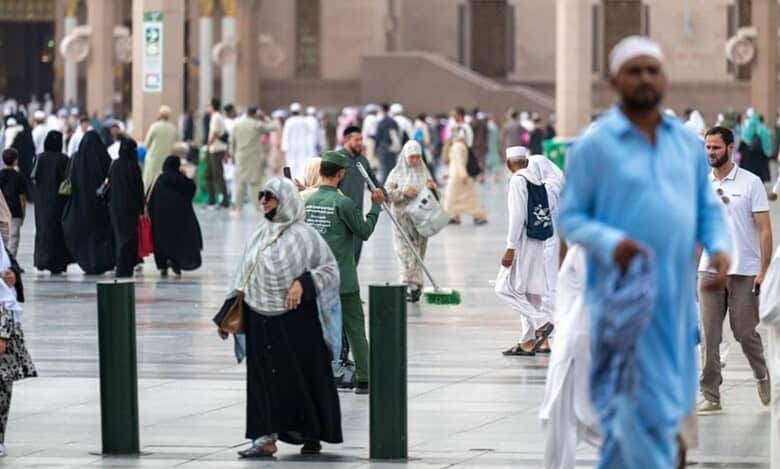 Bustling courtyard of Prophet's Mosque in Madinah with Umrah pilgrims and a cleaner amid iconic architecture.