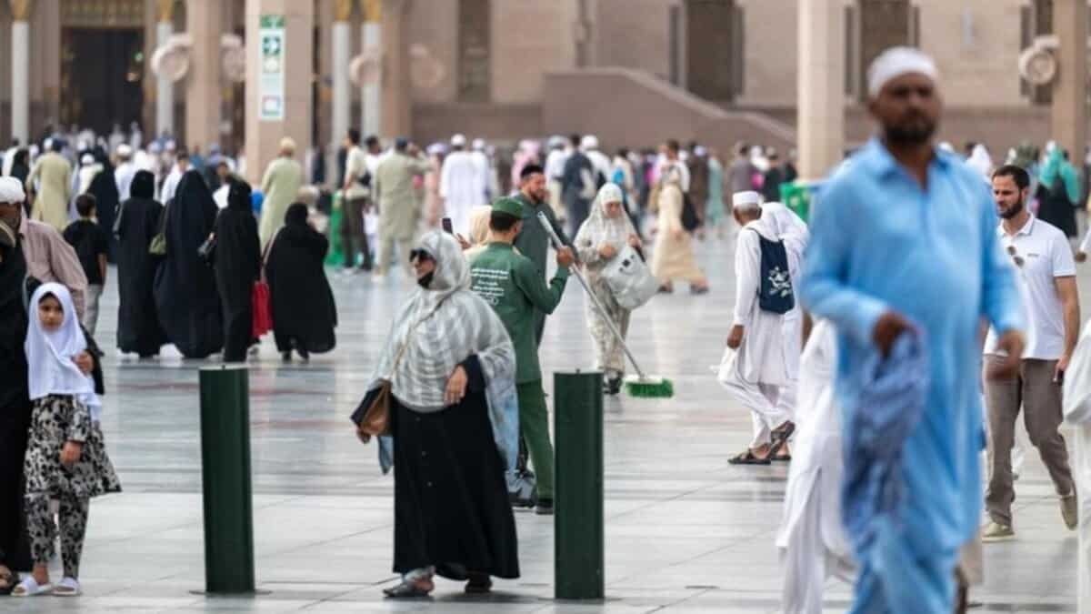Bustling courtyard of Prophet's Mosque in Madinah with Umrah pilgrims and a cleaner amid iconic architecture.