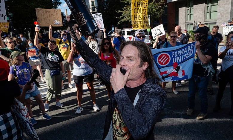A demonstrator yells into a megaphone with others in the street outside of the National Labor Relations Board (NLRB) headquarters,