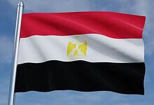 Flag of Egypt waving on a flagpole, featuring horizontal red, white, and black stripes with the golden Eagle of Saladin in the center.