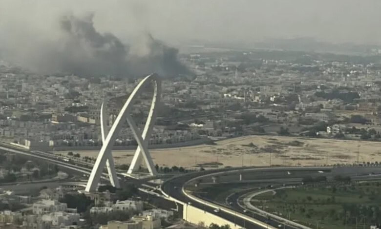Smoke rises over buildings in Doha near a landmark arch.