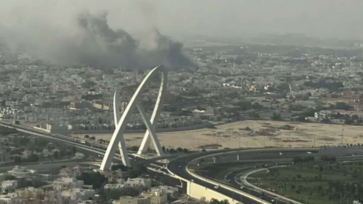 Smoke rises over buildings in Doha near a landmark arch.
