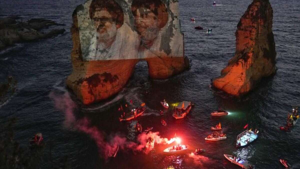 Image shows portraits of former Hezbollah leaders Hassan Nasrallah and Hashem Safieddine projected onto the Raouche sea rock during a commemorative event in Beirut, Lebanon, with boats and flares in the water, dated September 25, 2025.