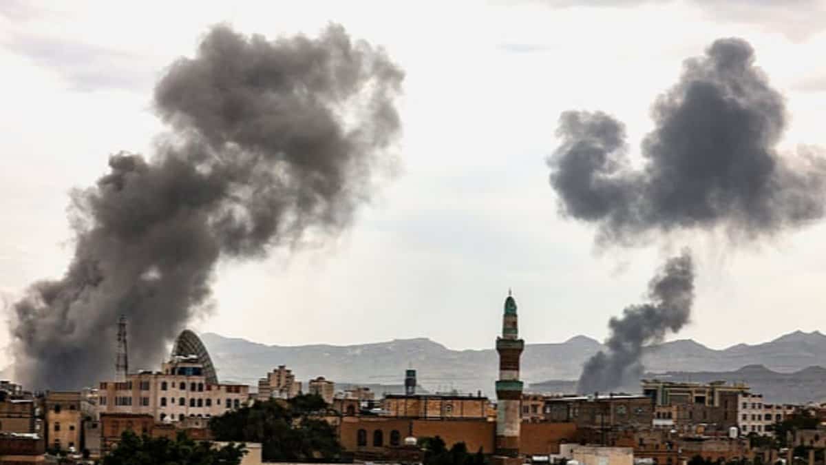Smoke rises over buildings following an airstrike in Sanaa, Yemen, with dark plumes visible against a cloudy sky.