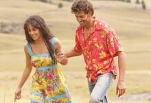 A couple joyfully walks hand-in-hand through a golden field, smiling and enjoying the sunny day.
